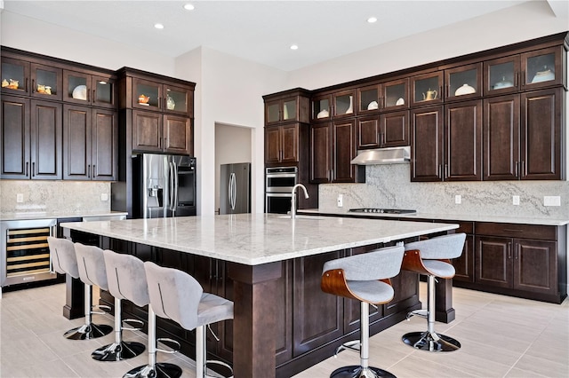 kitchen with decorative backsplash, appliances with stainless steel finishes, a sink, beverage cooler, and under cabinet range hood