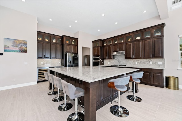 kitchen featuring wine cooler, under cabinet range hood, a spacious island, stainless steel refrigerator with ice dispenser, and black stovetop