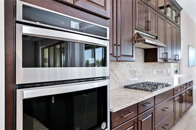 kitchen featuring stainless steel appliances, decorative backsplash, glass insert cabinets, dark brown cabinetry, and under cabinet range hood