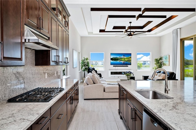 kitchen with open floor plan, a tray ceiling, stainless steel appliances, under cabinet range hood, and a sink