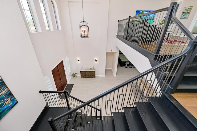 stairs with baseboards, wood finished floors, a towering ceiling, and an inviting chandelier