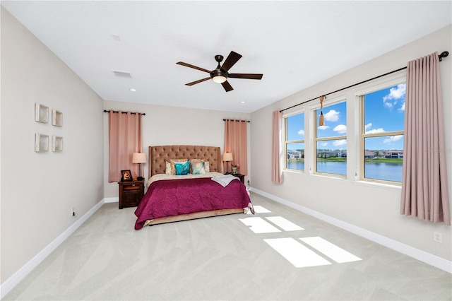 bedroom with light carpet, a water view, visible vents, and baseboards