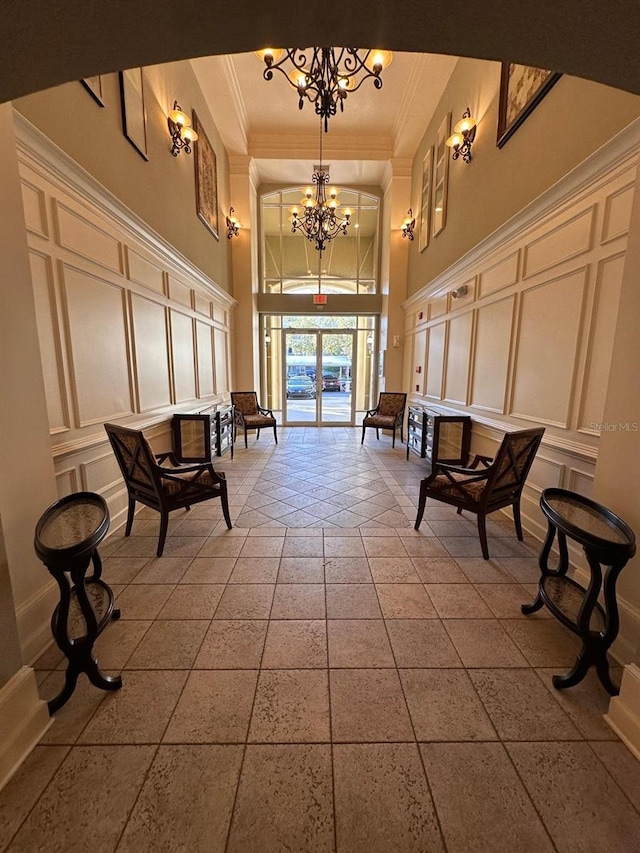 sitting room with a decorative wall, a towering ceiling, an inviting chandelier, and crown molding