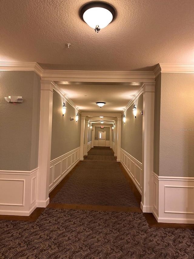 hallway featuring a decorative wall, ornamental molding, a wainscoted wall, and a textured ceiling