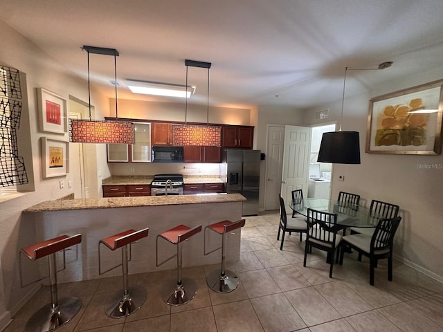 kitchen featuring hanging light fixtures, a peninsula, a kitchen bar, stainless steel appliances, and light stone counters