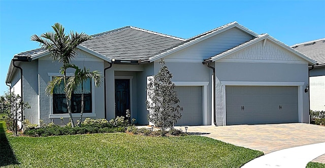 ranch-style house with a tile roof, an attached garage, decorative driveway, a front lawn, and stucco siding