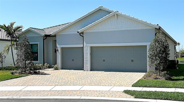 ranch-style house with decorative driveway, an attached garage, a tile roof, and stucco siding