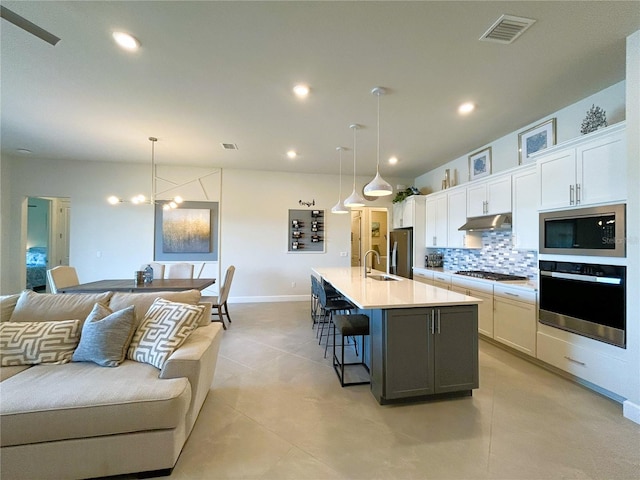 kitchen featuring visible vents, backsplash, appliances with stainless steel finishes, open floor plan, and under cabinet range hood