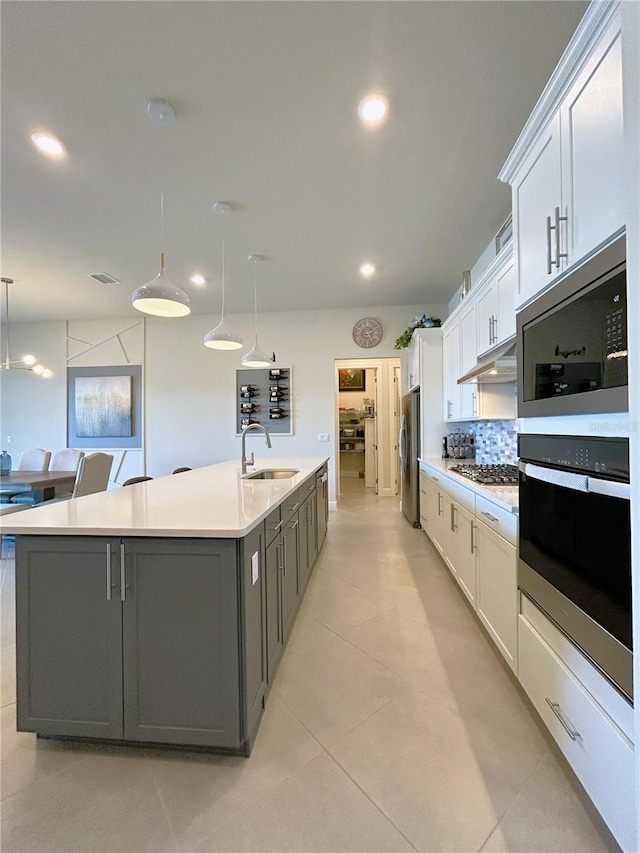 kitchen featuring appliances with stainless steel finishes, a sink, a large island with sink, and white cabinetry