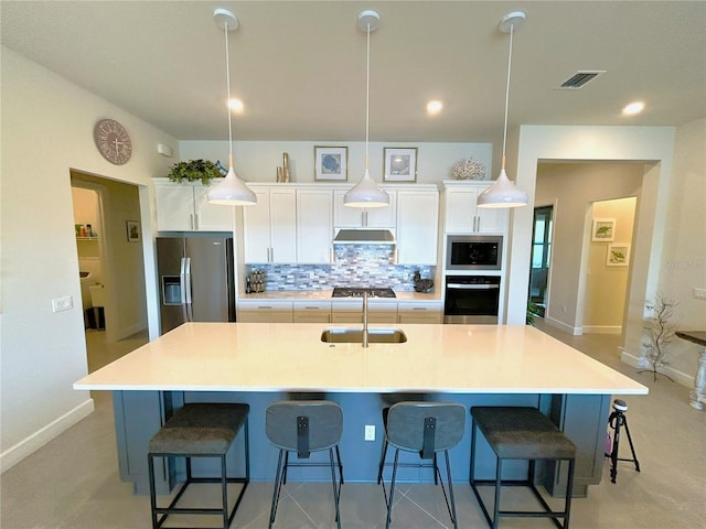 kitchen with under cabinet range hood, stainless steel appliances, a sink, visible vents, and decorative backsplash