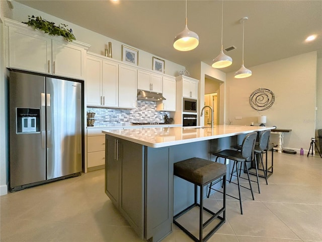 kitchen with a spacious island, tasteful backsplash, appliances with stainless steel finishes, white cabinets, and under cabinet range hood