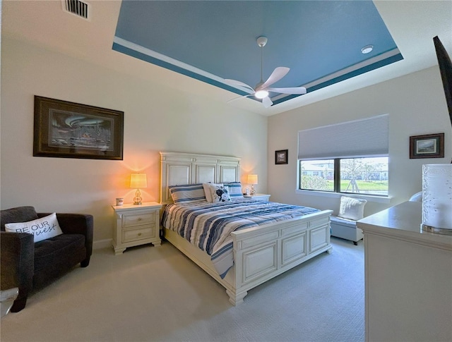 bedroom with ceiling fan, visible vents, a raised ceiling, and light colored carpet