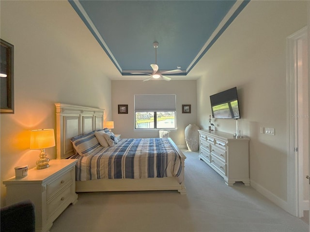 bedroom featuring a ceiling fan, a tray ceiling, light colored carpet, and baseboards