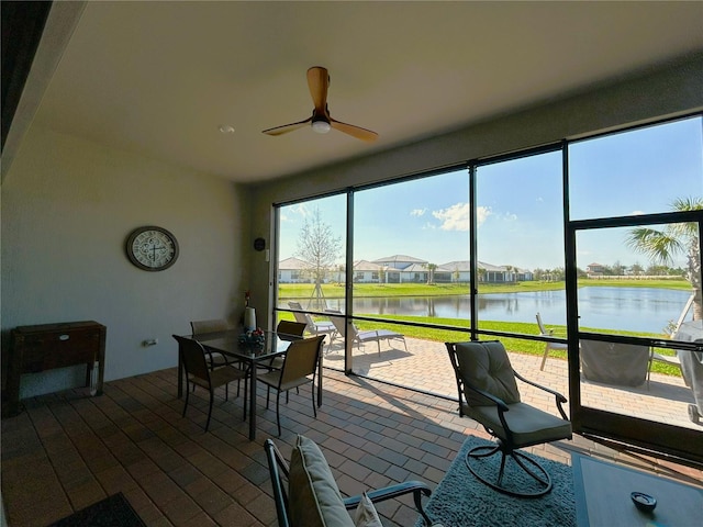 sunroom with ceiling fan and a water view