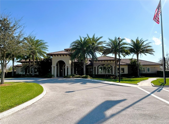 view of front of property featuring a tiled roof, curved driveway, a front yard, and stucco siding