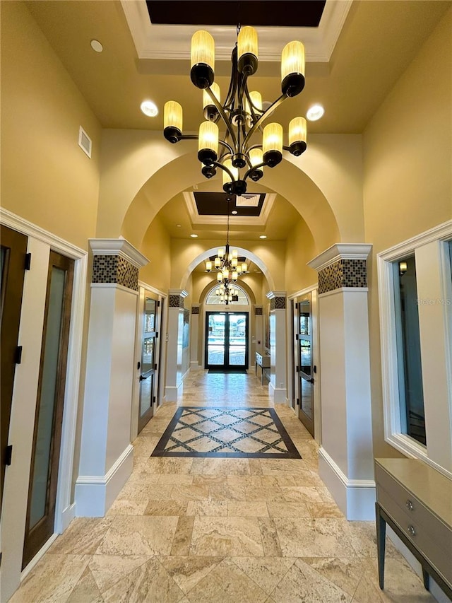 corridor featuring a chandelier, arched walkways, a towering ceiling, french doors, and a raised ceiling