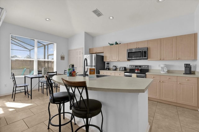 kitchen featuring light brown cabinets, stainless steel appliances, visible vents, a kitchen breakfast bar, and light countertops