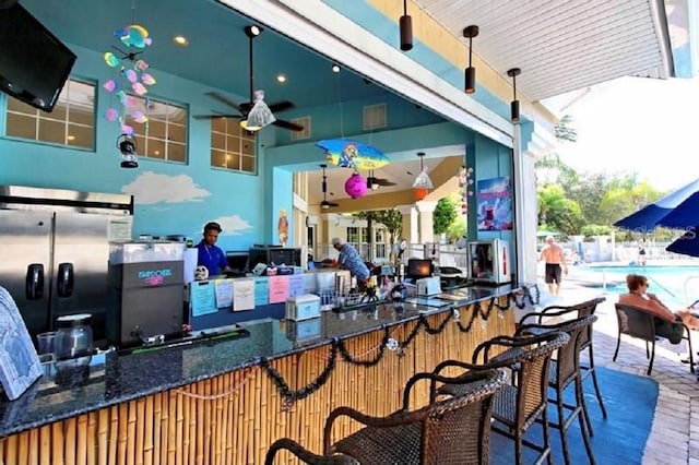view of patio with a community pool, fence, a ceiling fan, and outdoor wet bar
