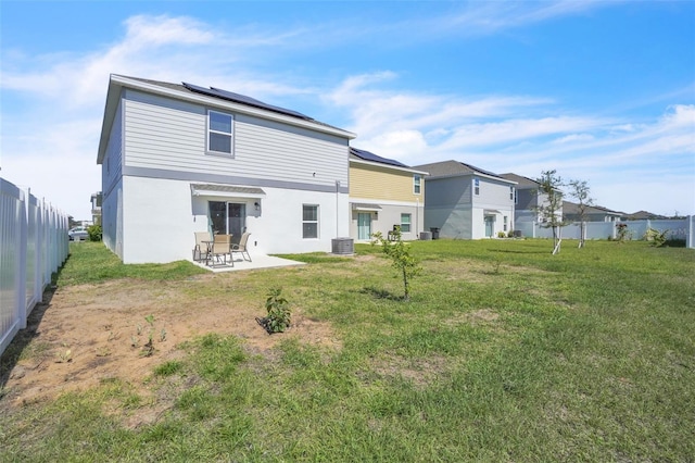 rear view of house with a lawn, roof mounted solar panels, a patio area, fence, and cooling unit