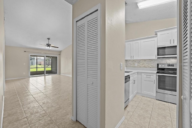 kitchen with light tile patterned flooring, white cabinets, open floor plan, appliances with stainless steel finishes, and tasteful backsplash