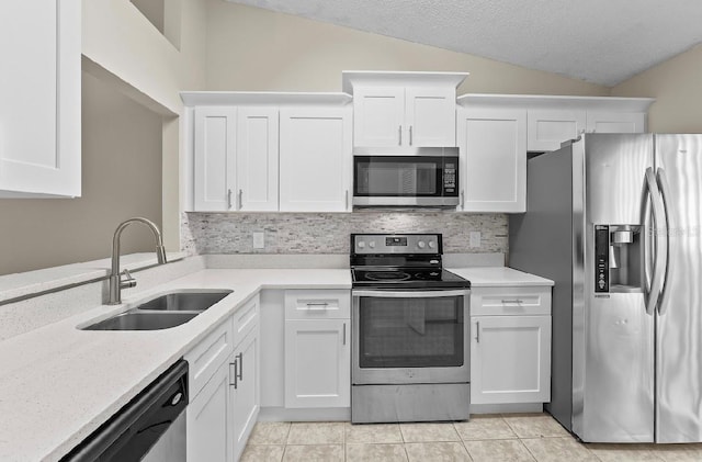 kitchen with lofted ceiling, light tile patterned floors, stainless steel appliances, a sink, and white cabinets