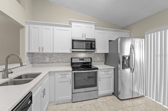 kitchen with light tile patterned floors, stainless steel appliances, a sink, white cabinets, and vaulted ceiling