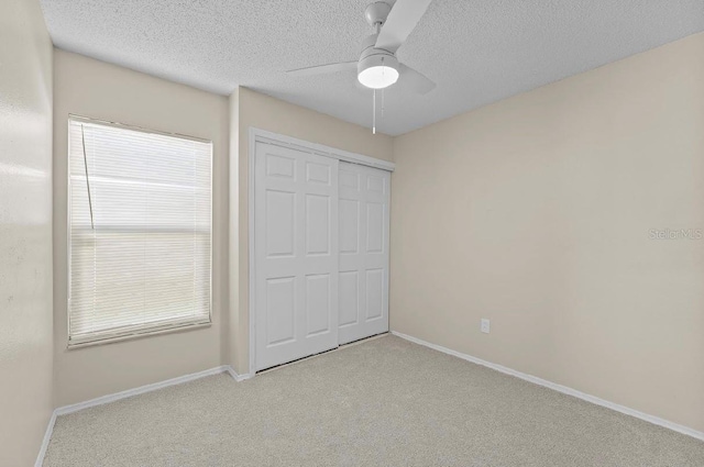 unfurnished bedroom with a textured ceiling, ceiling fan, baseboards, a closet, and carpet