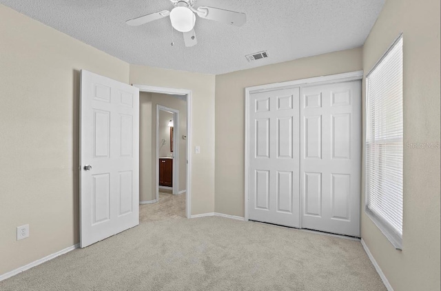 unfurnished bedroom featuring a textured ceiling, carpet flooring, visible vents, baseboards, and a closet