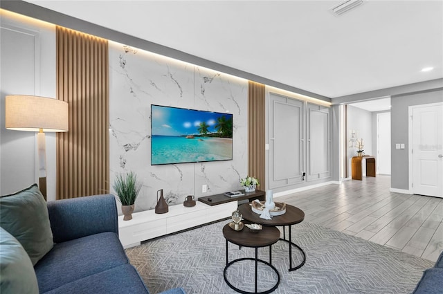 living area with baseboards, an accent wall, visible vents, and wood finished floors