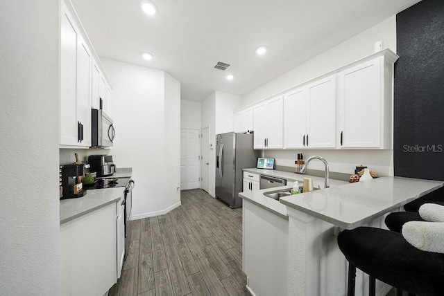 kitchen featuring appliances with stainless steel finishes, white cabinetry, a sink, and wood finished floors