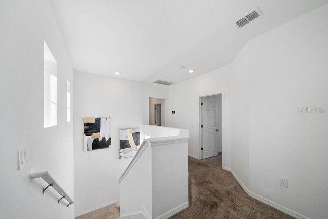 hallway featuring carpet, visible vents, baseboards, and an upstairs landing