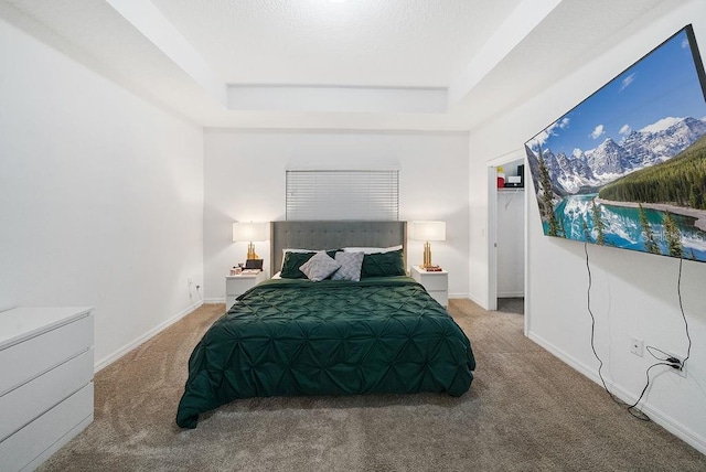 carpeted bedroom featuring a raised ceiling, a walk in closet, and baseboards