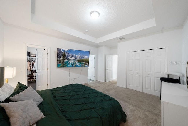 bedroom featuring carpet floors, a tray ceiling, a closet, visible vents, and a textured ceiling