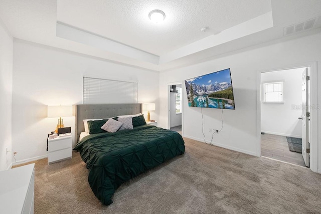 carpeted bedroom featuring a textured ceiling, a tray ceiling, visible vents, and baseboards