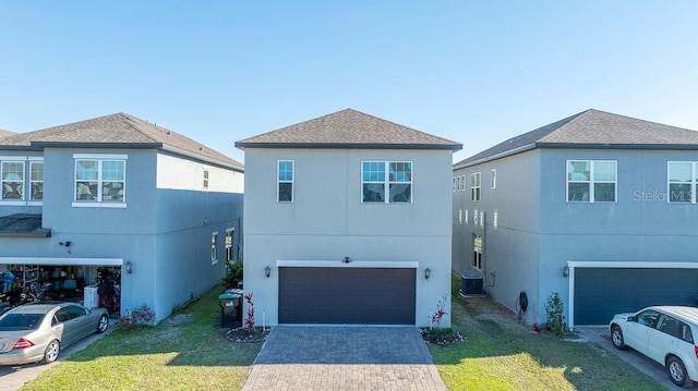 view of front of house featuring a garage, decorative driveway, a front lawn, and central AC unit