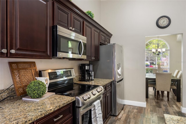 kitchen with light stone counters, wood finished floors, dark brown cabinets, appliances with stainless steel finishes, and a chandelier