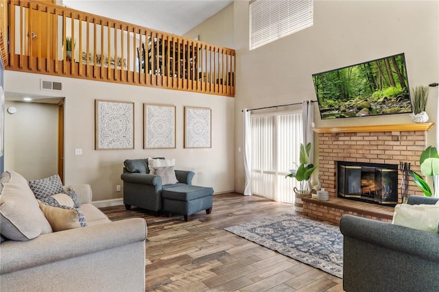 living area with visible vents, a brick fireplace, baseboards, a high ceiling, and wood finished floors