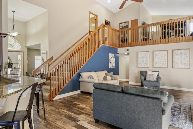 living area with a ceiling fan, dark wood-style floors, stairway, baseboards, and a towering ceiling