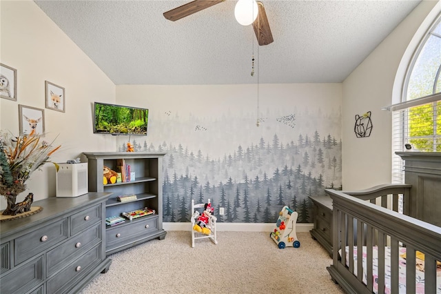 carpeted bedroom featuring a crib, baseboards, vaulted ceiling, a textured ceiling, and a ceiling fan