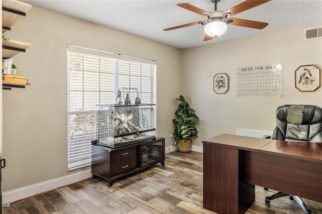 office space with visible vents, a textured ceiling, wood finished floors, baseboards, and ceiling fan