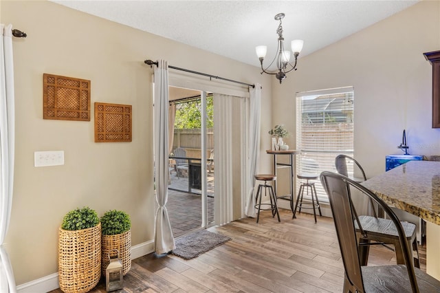 dining room with light wood finished floors, baseboards, a chandelier, lofted ceiling, and a textured ceiling