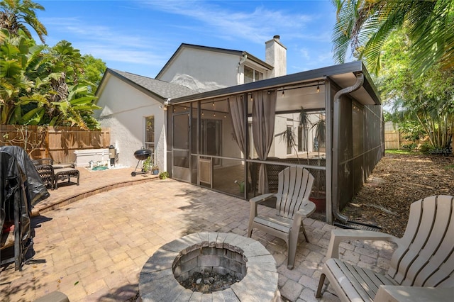 view of patio / terrace with grilling area, a fenced backyard, a sunroom, and an outdoor fire pit