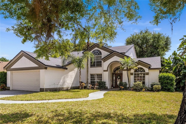 traditional-style house with stucco siding, driveway, a front lawn, roof with shingles, and a garage