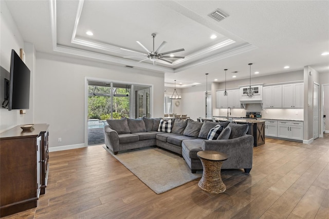 living room with a raised ceiling, visible vents, ceiling fan, and light wood-style flooring