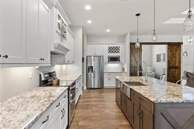 kitchen featuring white cabinets, a barn door, stainless steel appliances, and a sink