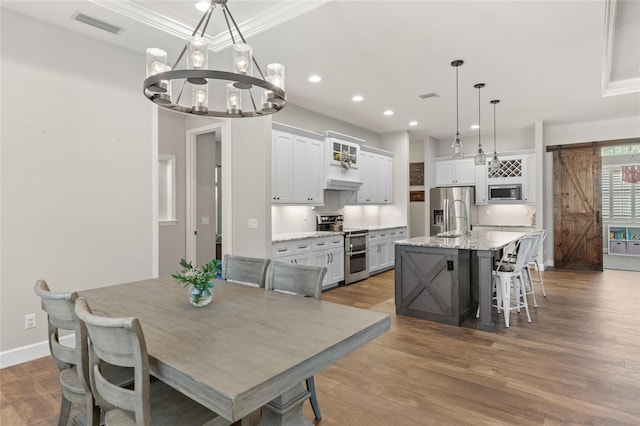 dining room featuring a barn door, wood finished floors, visible vents, and recessed lighting