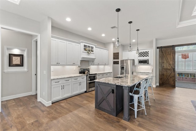 kitchen featuring a barn door, white cabinets, a breakfast bar area, dark wood-style flooring, and stainless steel appliances