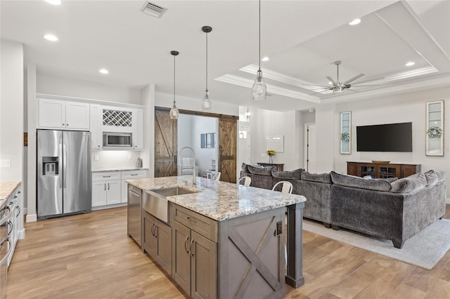 kitchen with a barn door, stainless steel appliances, a sink, visible vents, and light wood finished floors