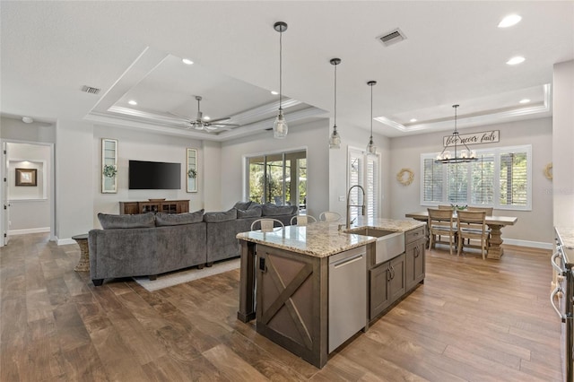 kitchen featuring a raised ceiling, visible vents, stainless steel dishwasher, a sink, and wood finished floors