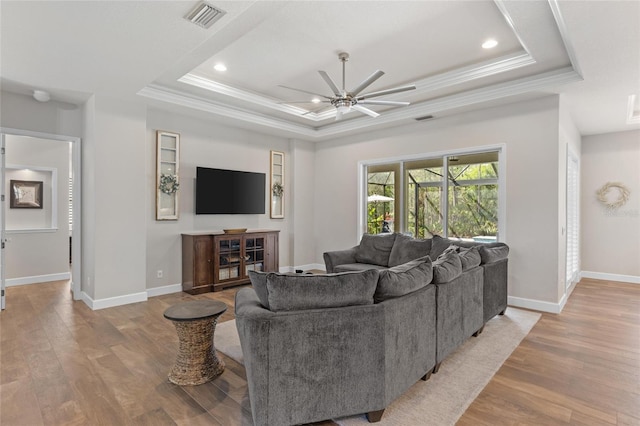 living room with visible vents, a tray ceiling, light wood-style flooring, and ornamental molding